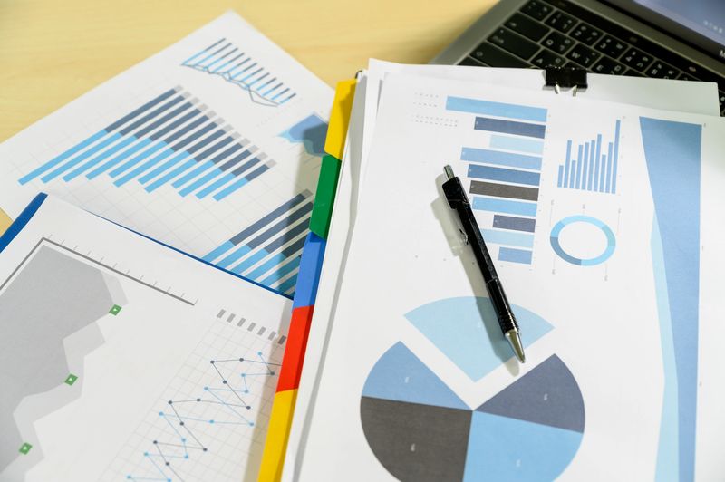 Pen placed on financial charts and graphs near a laptop keyboard.